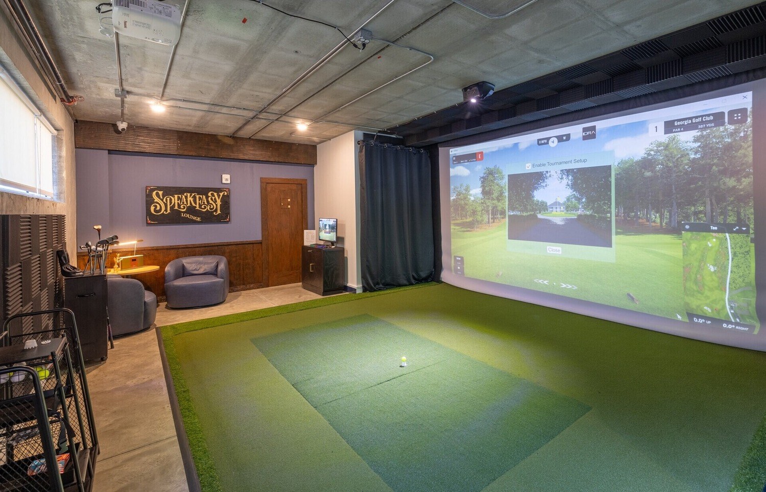 Multi-family amenity golf simulator room with projection screen, turf hitting bay, lounge seating and acoustic wall treatment