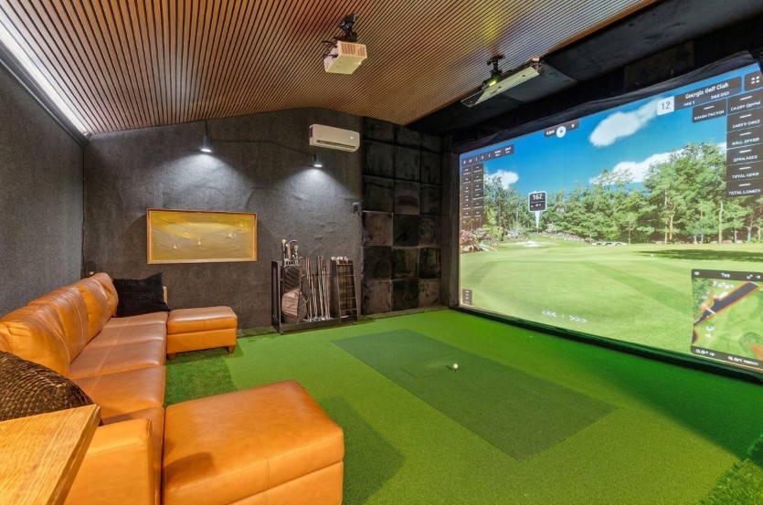 Residential golf simulator room with impact screen, turf hitting area, leather sectional seating and wood slat ceiling