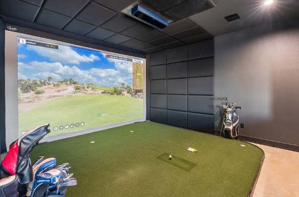 Residential golf simulator room with impact screen, putting green turf, padded acoustic wall panels and club storage